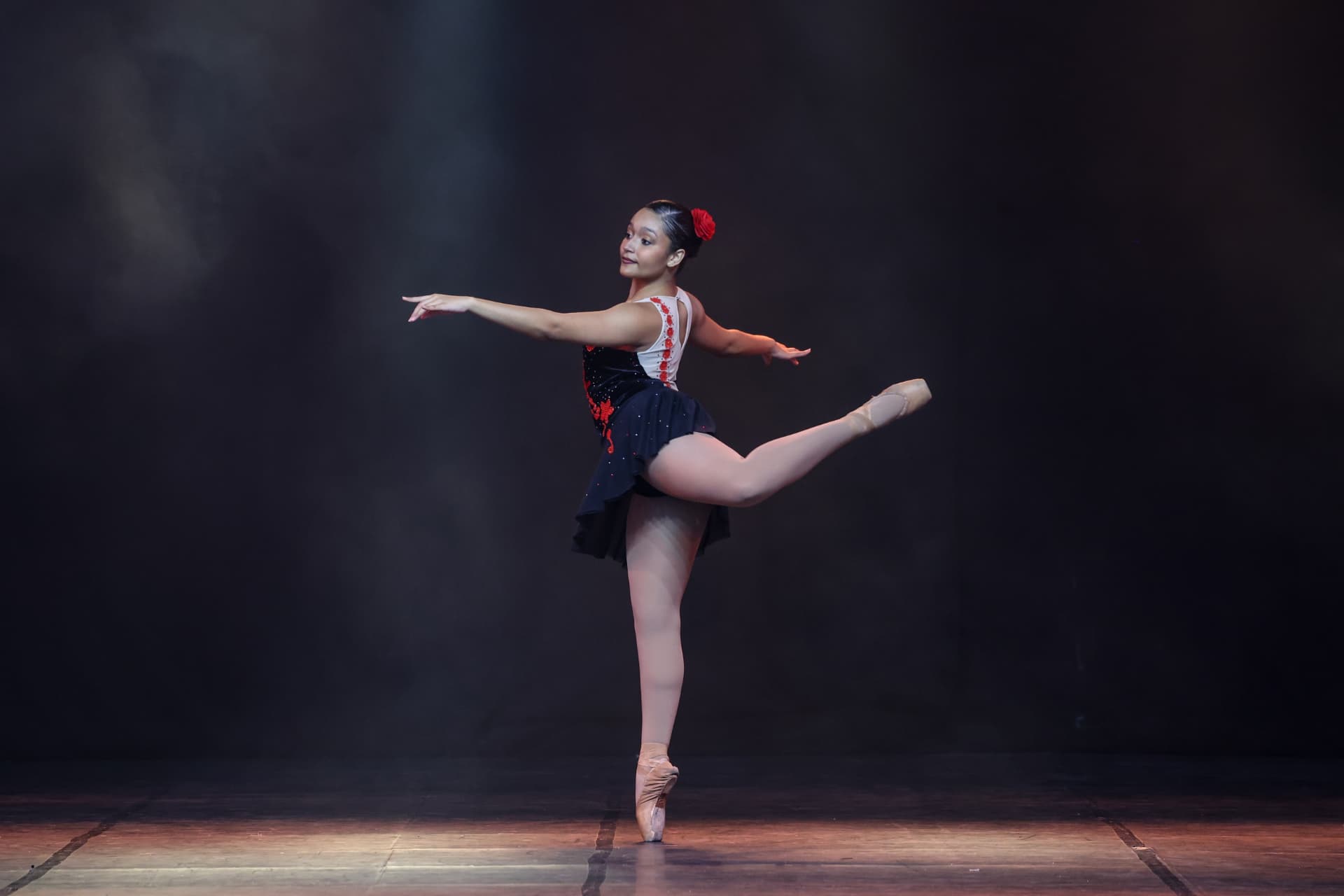 Bailarina em pointe tendu no palco, figurino preto e vermelho