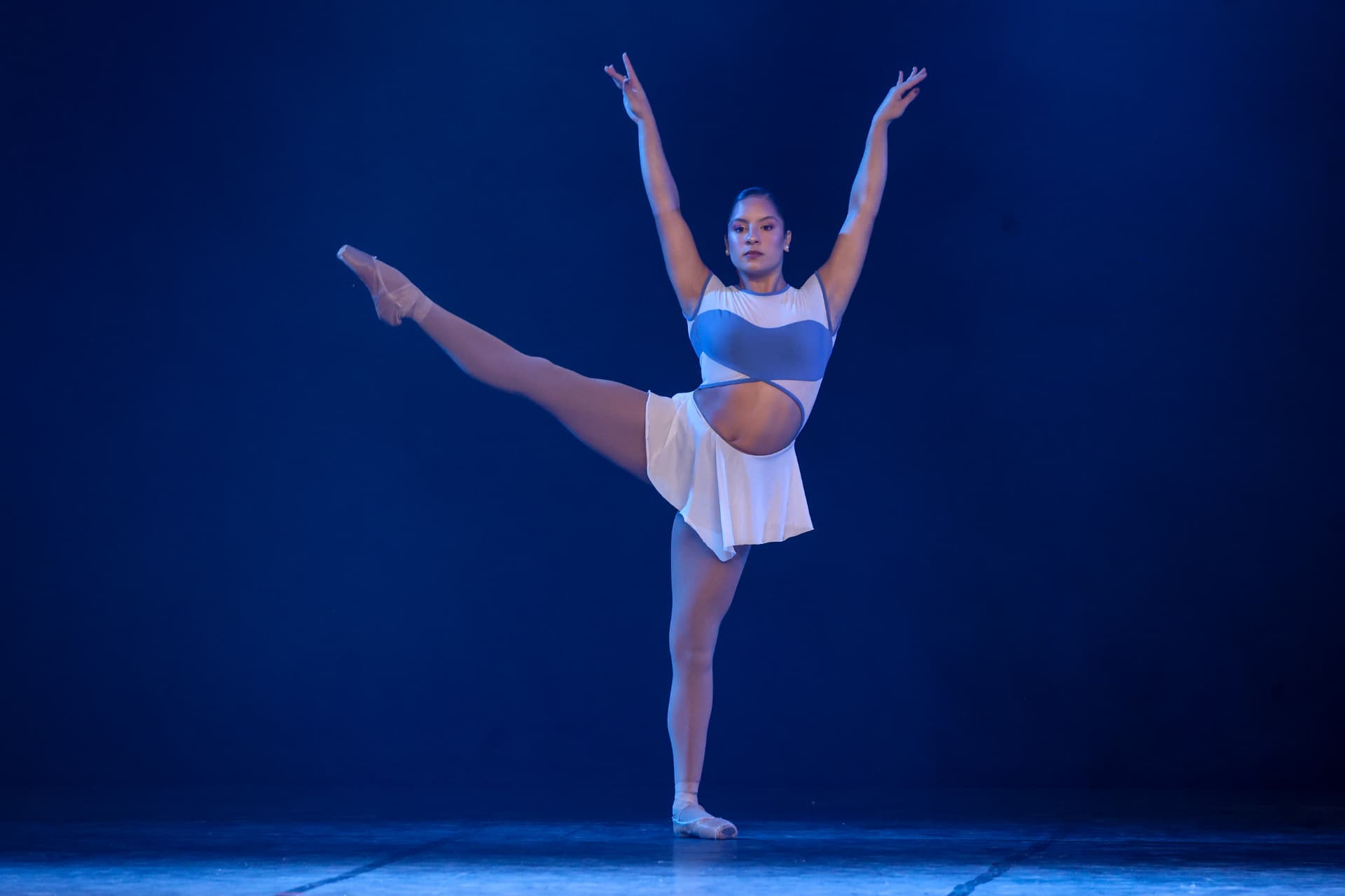 Bailarina com braços erguidos sob luz azul no palco